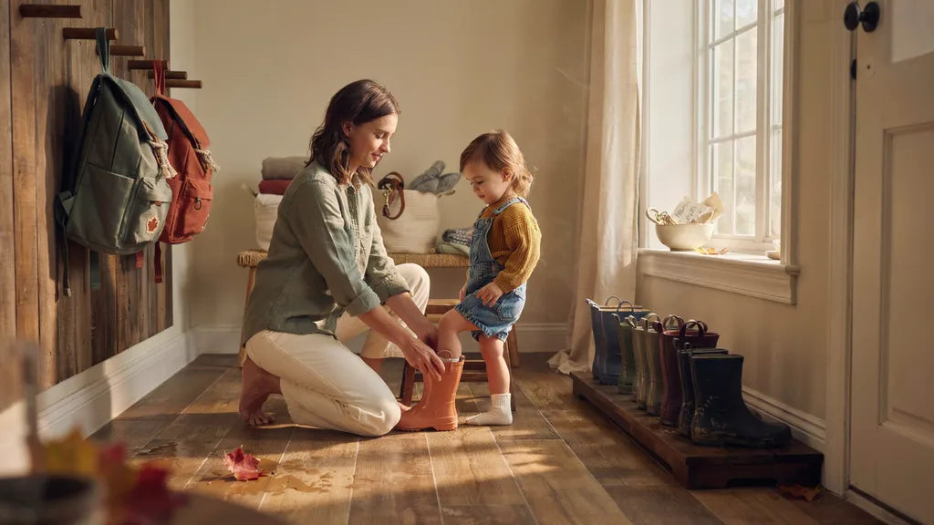 A parent and child in a cozy terracotta and sage Canadian mudroom, boots on a tray and backpacks on wooden hooks