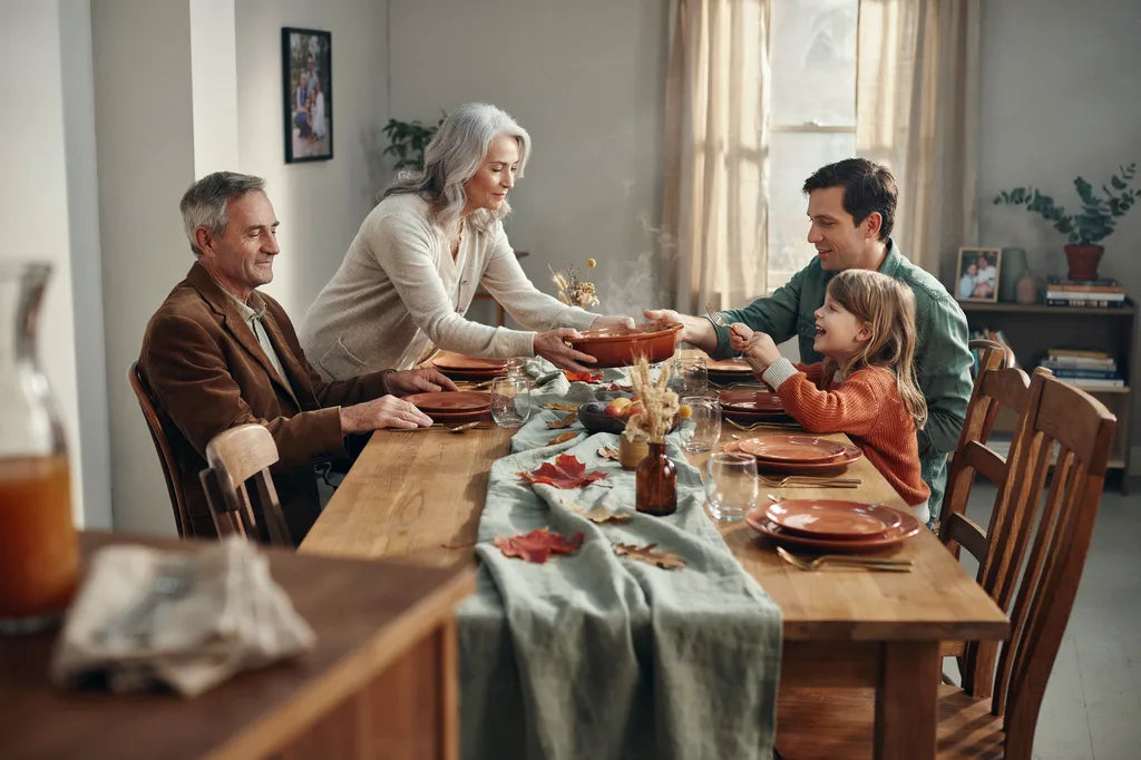 A Canadian family laughing around a Thanksgiving dinner table with extra chairs pulled up, in a warm terracotta and sage toned dining room.